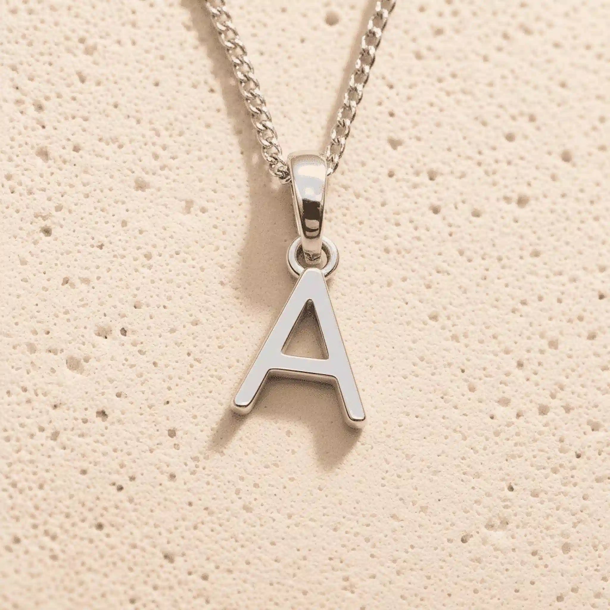 Sterling Silver Initial Necklace with a minimalist A charm pendant on a light stone background