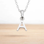 Sterling silver initial Necklace with a minimalistic 'A' initial letter pendant hanging above a light wooden surface