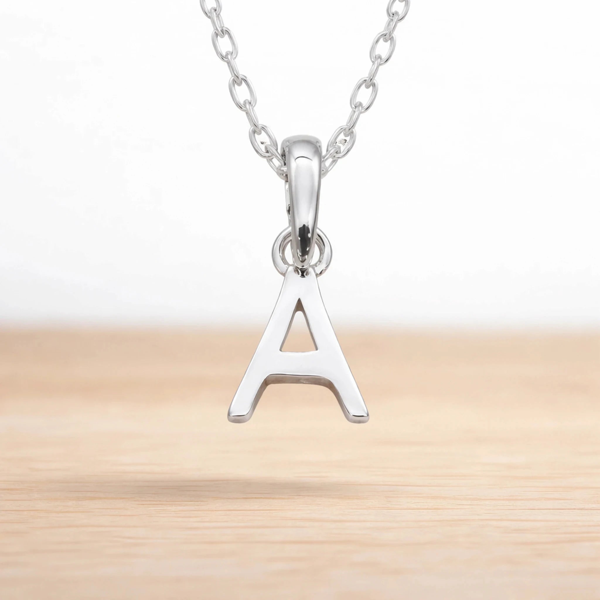 Sterling silver initial Necklace with a minimalistic 'A' initial letter pendant hanging above a light wooden surface