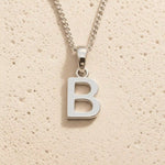 Sterling Silver Initial Necklace with a minimalist B charm pendant on a light stone background