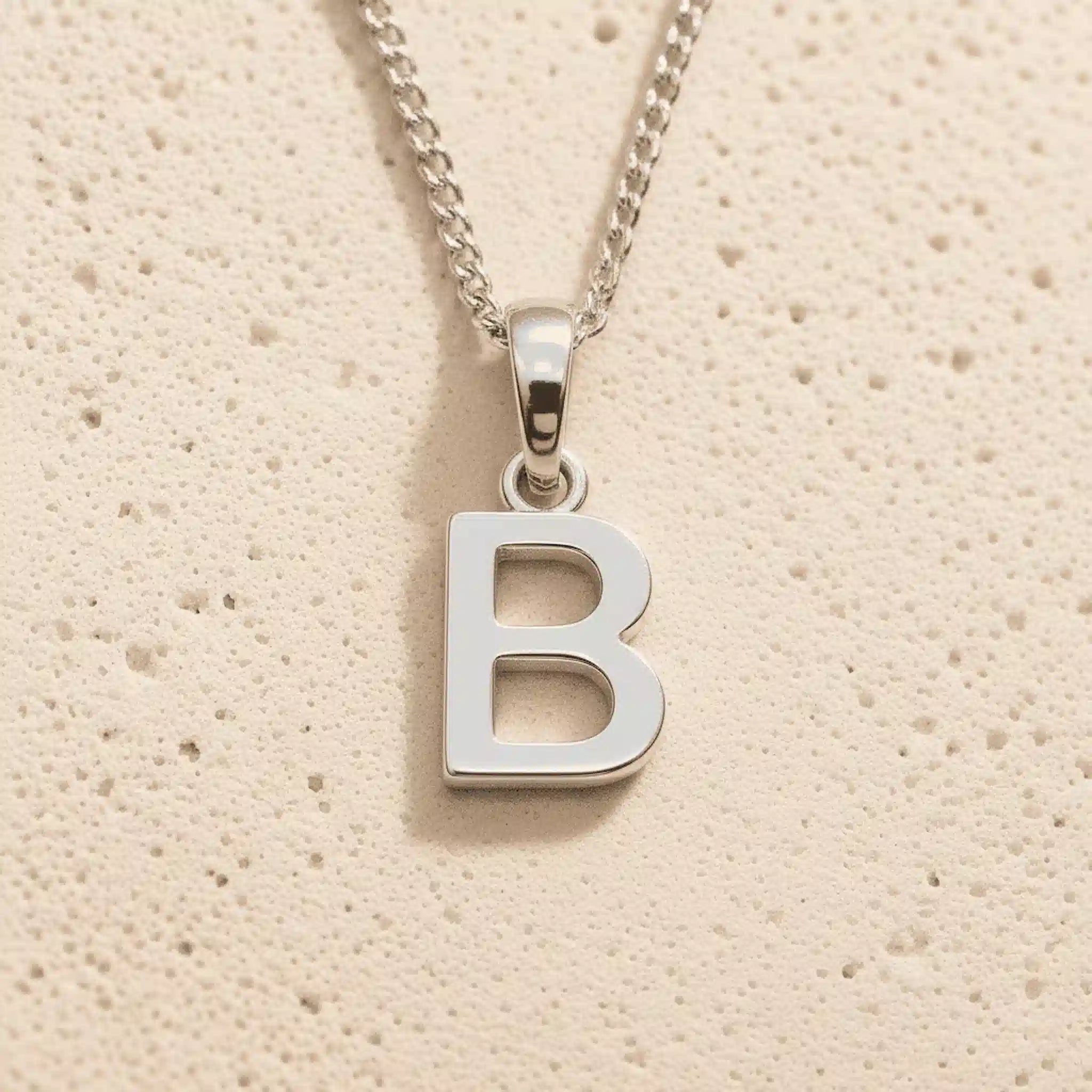 Sterling Silver Initial Necklace with a minimalist B charm pendant on a light stone background