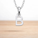 Sterling silver initial Necklace with a minimalist 'B' initial letter pendant hanging above a light wooden surface