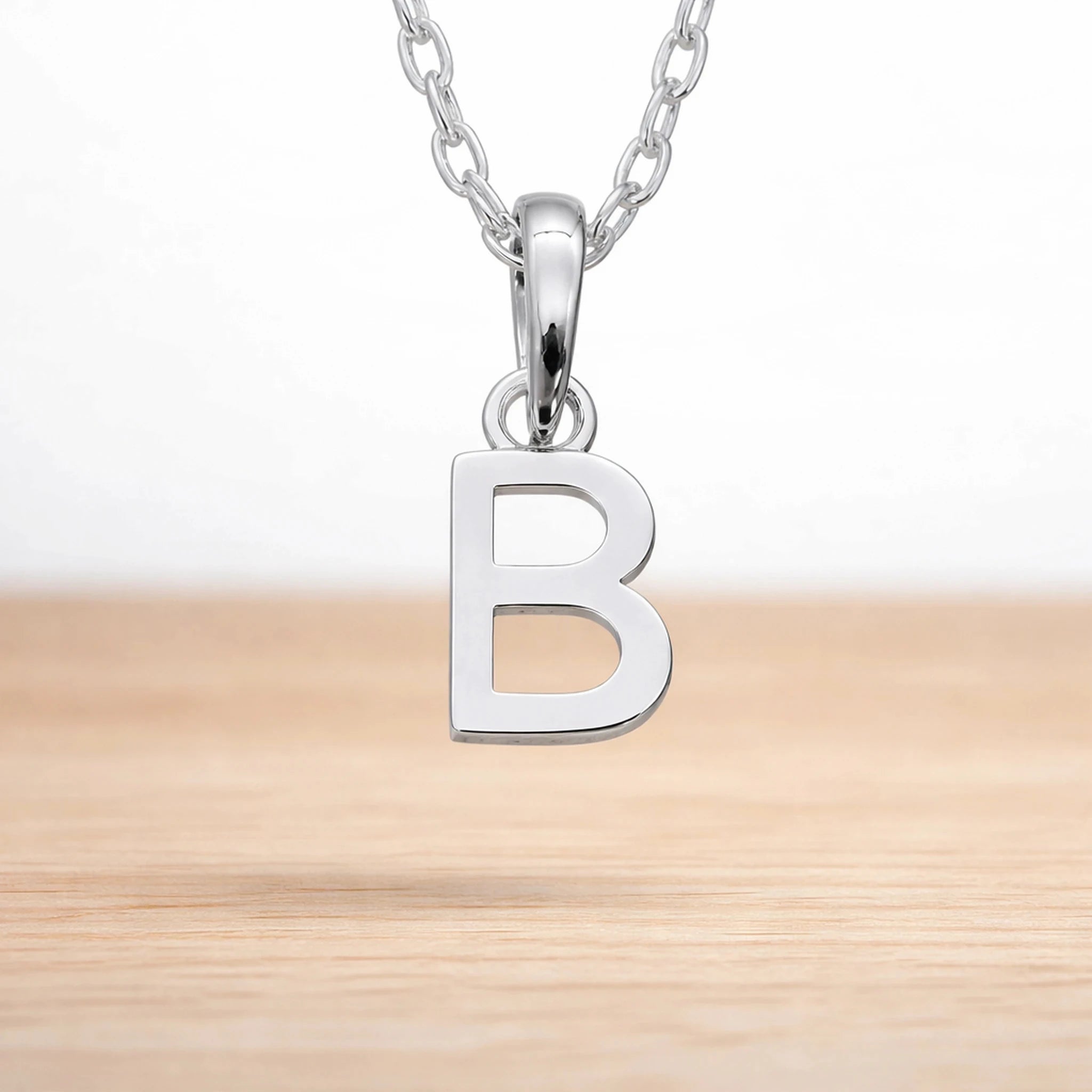 Sterling silver initial Necklace with a minimalist 'B' initial letter pendant hanging above a light wooden surface
