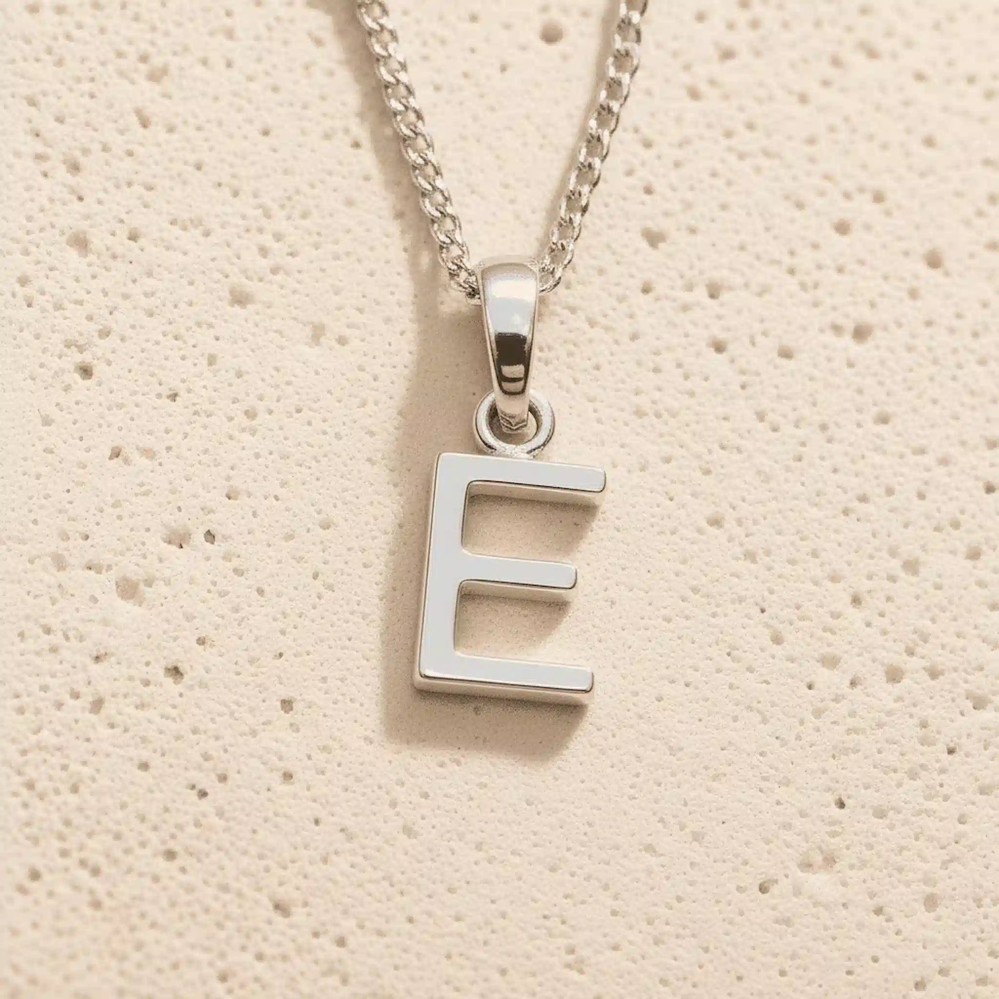 Sterling Silver Initial Necklace with a minimalist E charm pendant on a light stone background