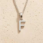 Sterling Silver Initial Necklace with a minimalist F charm pendant on a light stone background