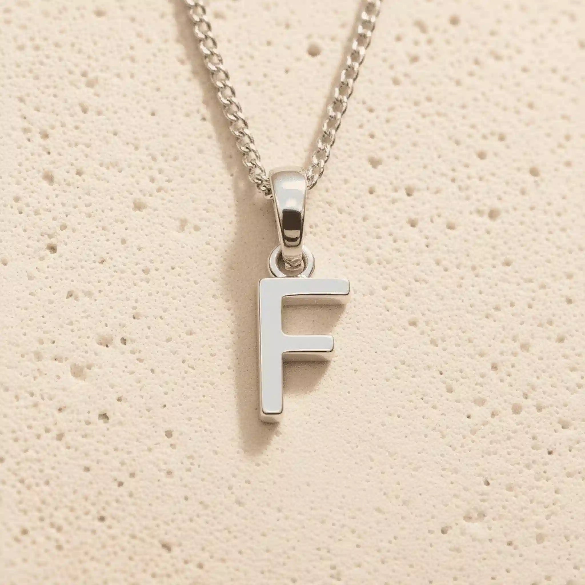 Sterling Silver Initial Necklace with a minimalist F charm pendant on a light stone background