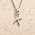 Sterling Silver Initial Necklace with a minimalist K charm pendant on a light stone background