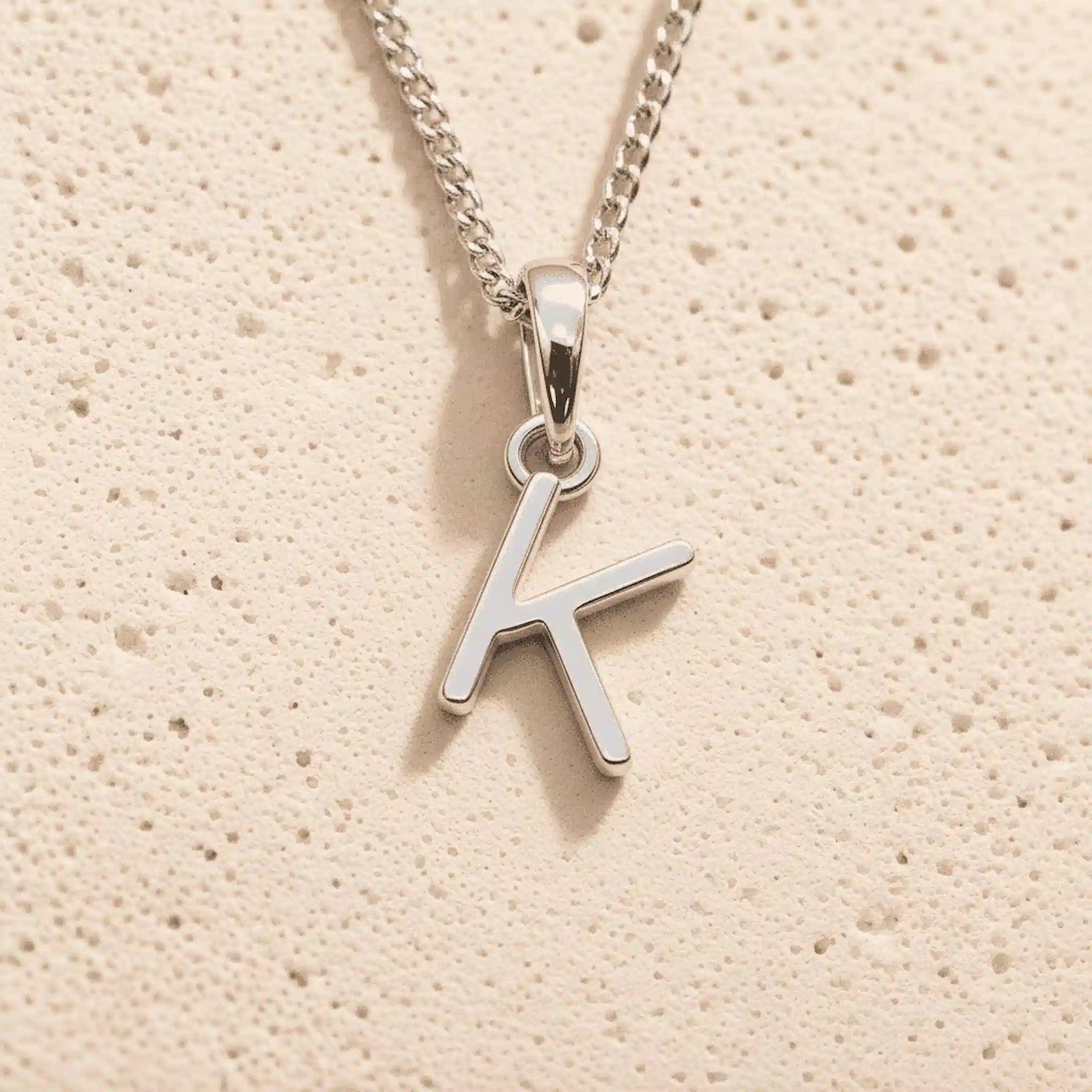 Sterling Silver Initial Necklace with a minimalist K charm pendant on a light stone background