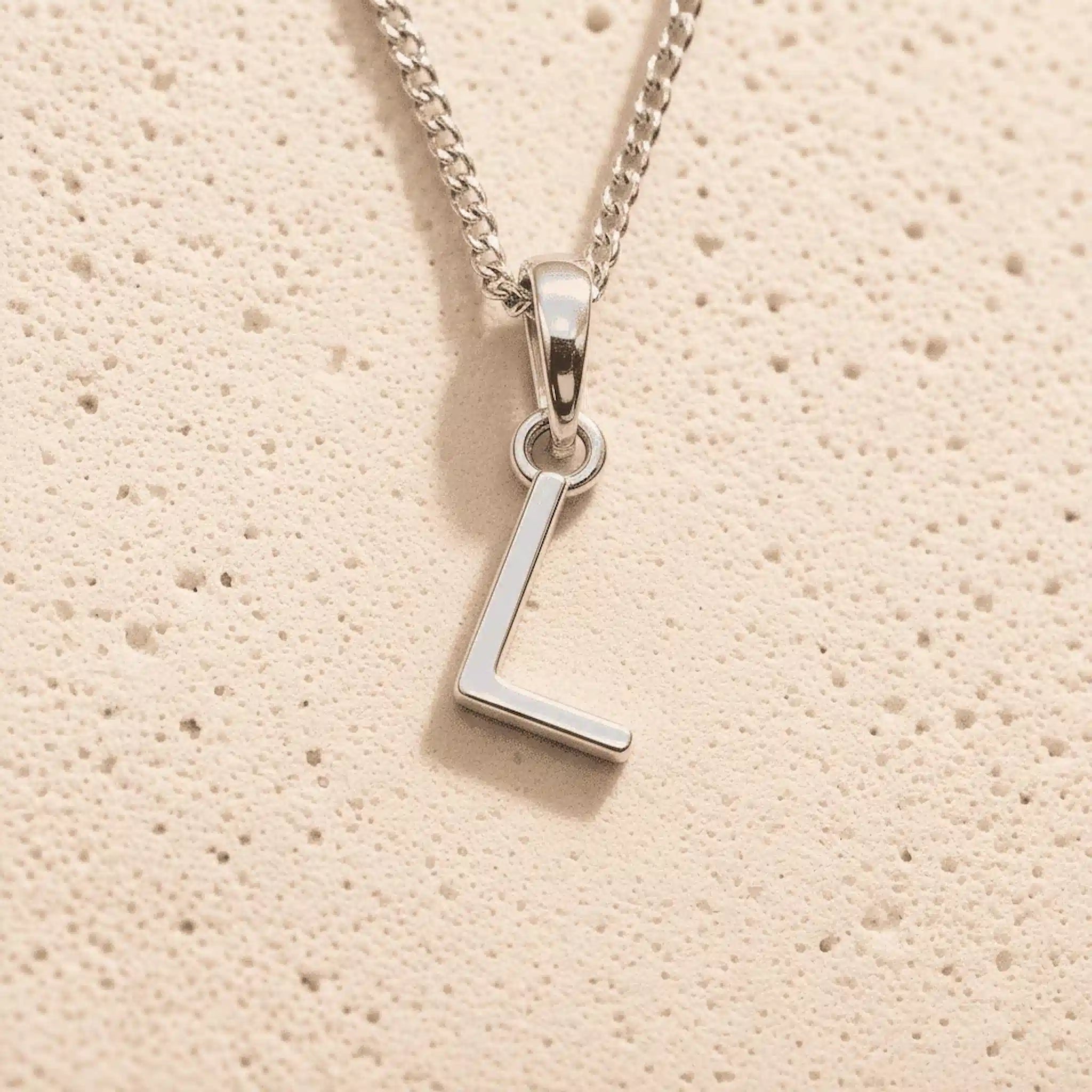 Sterling Silver Initial Necklace with a minimalist L charm pendant on a light stone background