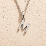 Sterling Silver Initial Necklace with a minimalist M charm pendant on a light stone background