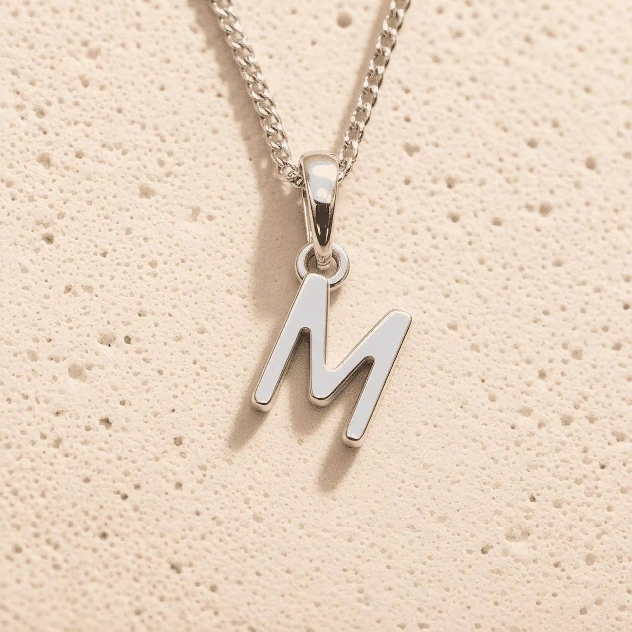 Sterling Silver Initial Necklace with a minimalist M charm pendant on a light stone background