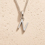 Sterling Silver Initial Necklace with a minimalist N charm pendant on a light stone background