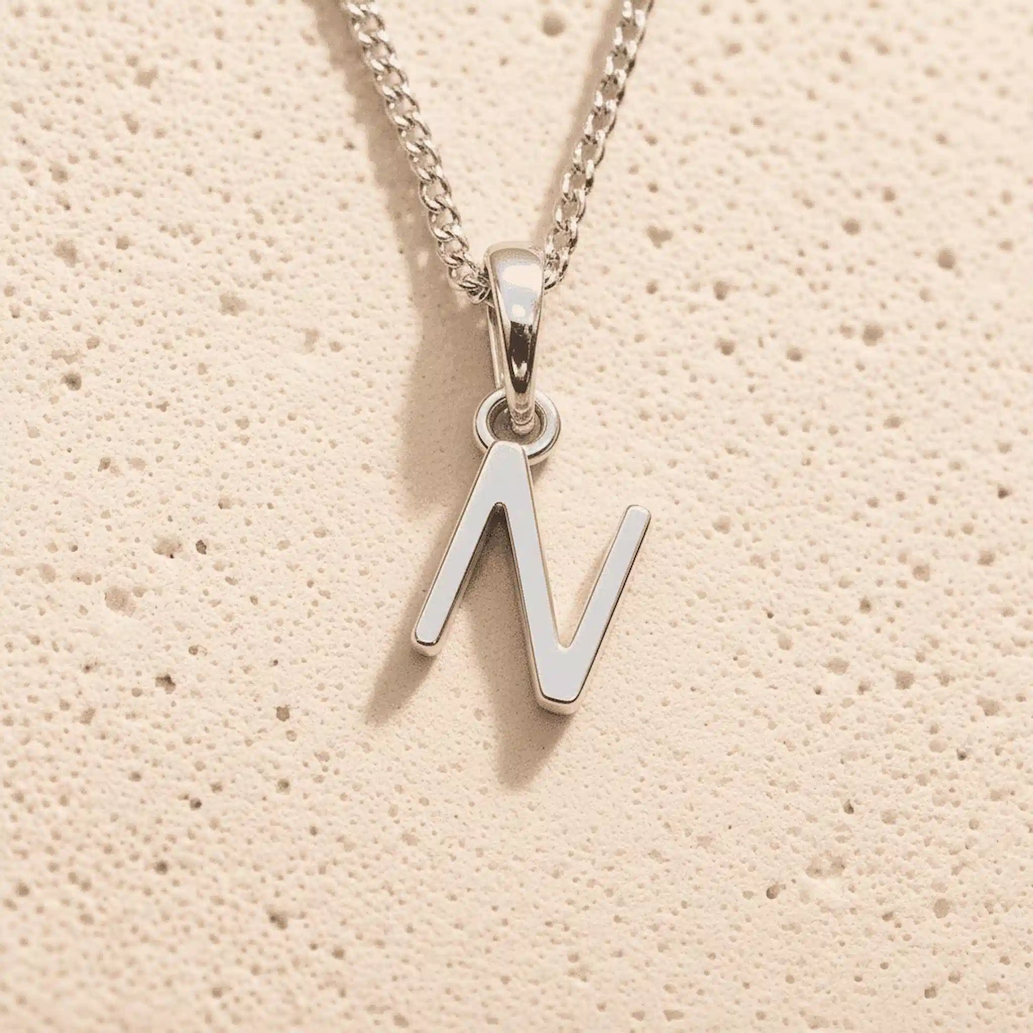 Sterling Silver Initial Necklace with a minimalist N charm pendant on a light stone background