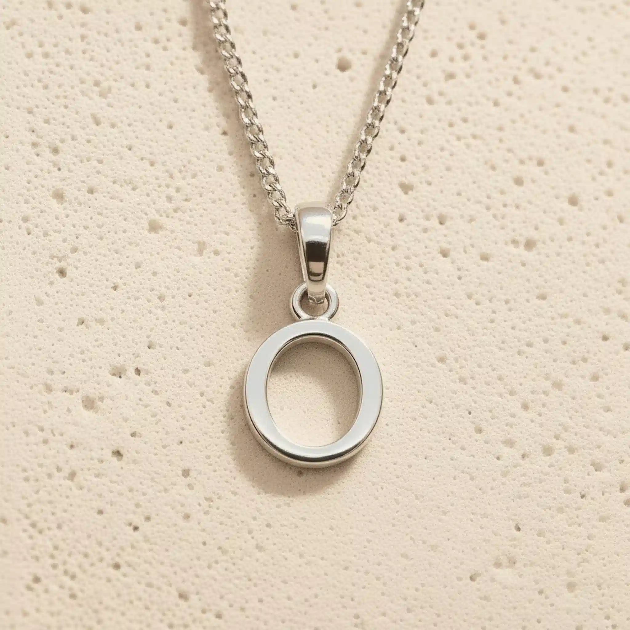 Sterling Silver Initial Necklace with a minimalist O charm pendant on a light stone background
