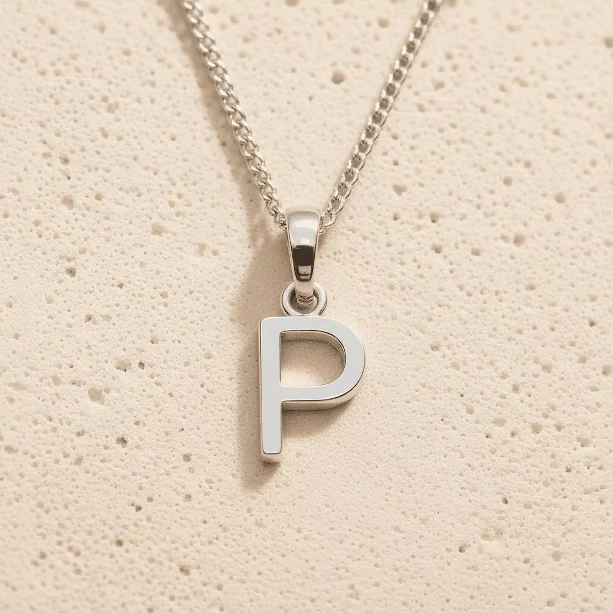 Sterling Silver Initial Necklace with a minimalist P charm pendant on a light stone background