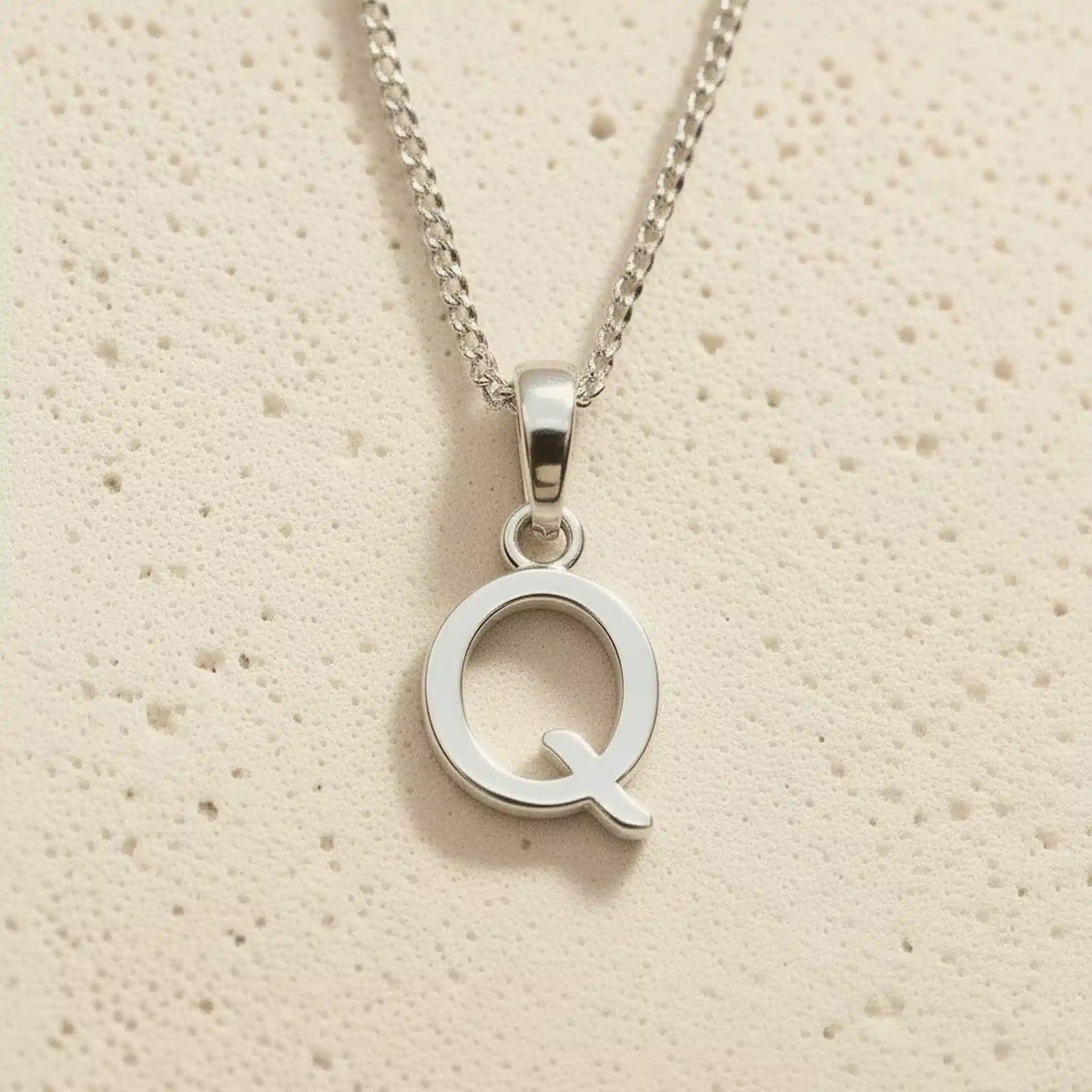Sterling Silver Initial Necklace with a minimalist Q charm pendant on a light stone background
