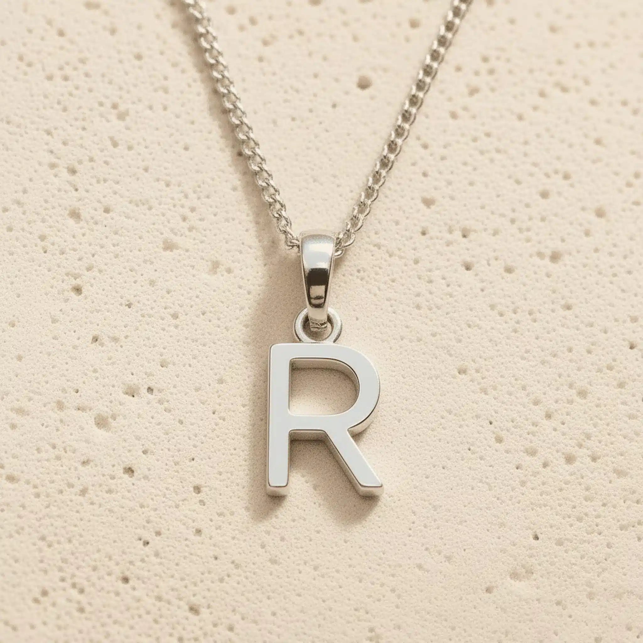Sterling Silver Initial Necklace with a minimalist R charm pendant on a light stone background
