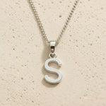 Sterling Silver Initial Necklace with a minimalist S charm pendant on a light stone background