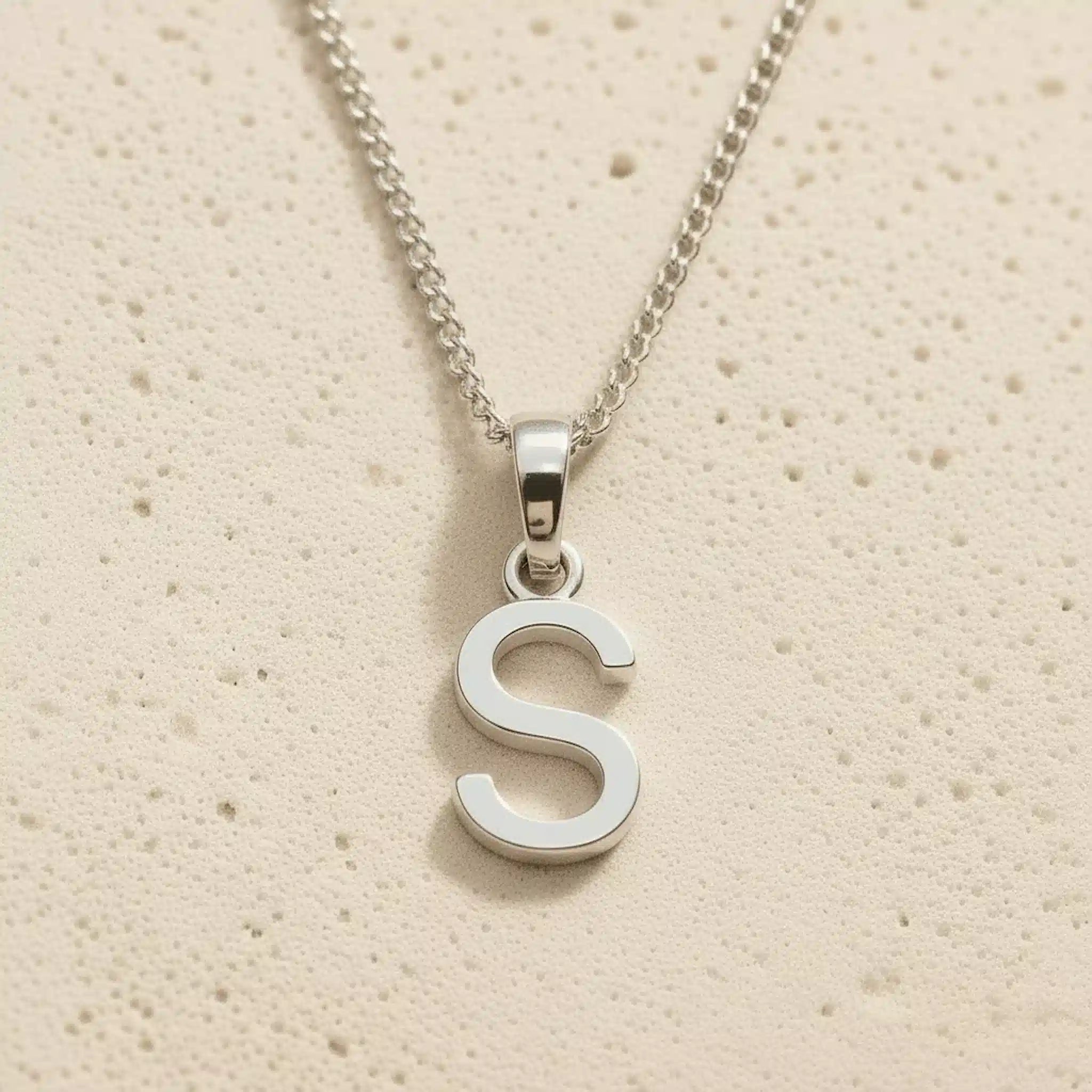 Sterling Silver Initial Necklace with a minimalist S charm pendant on a light stone background