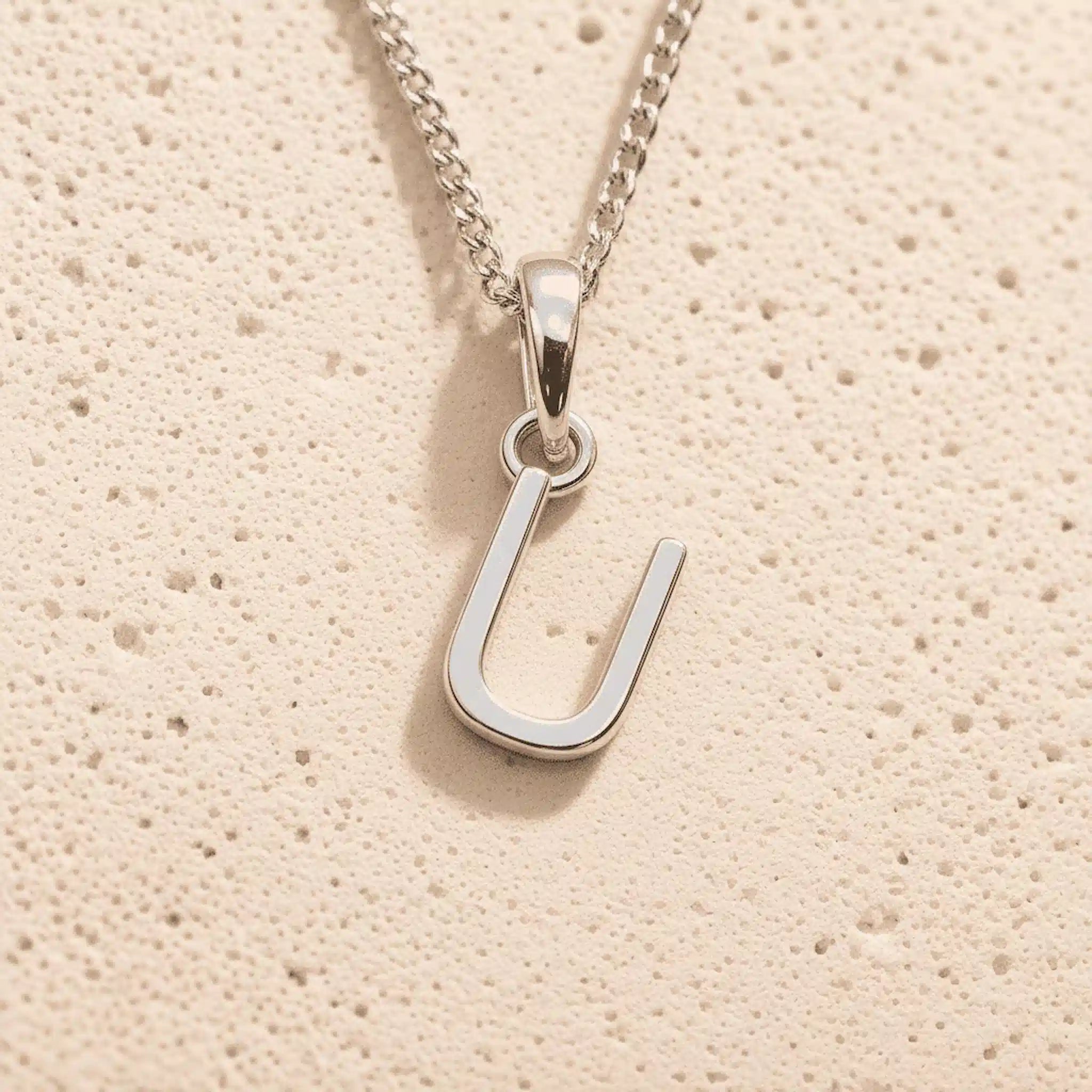 Sterling Silver Initial Necklace with a minimalist U charm pendant on a light stone background