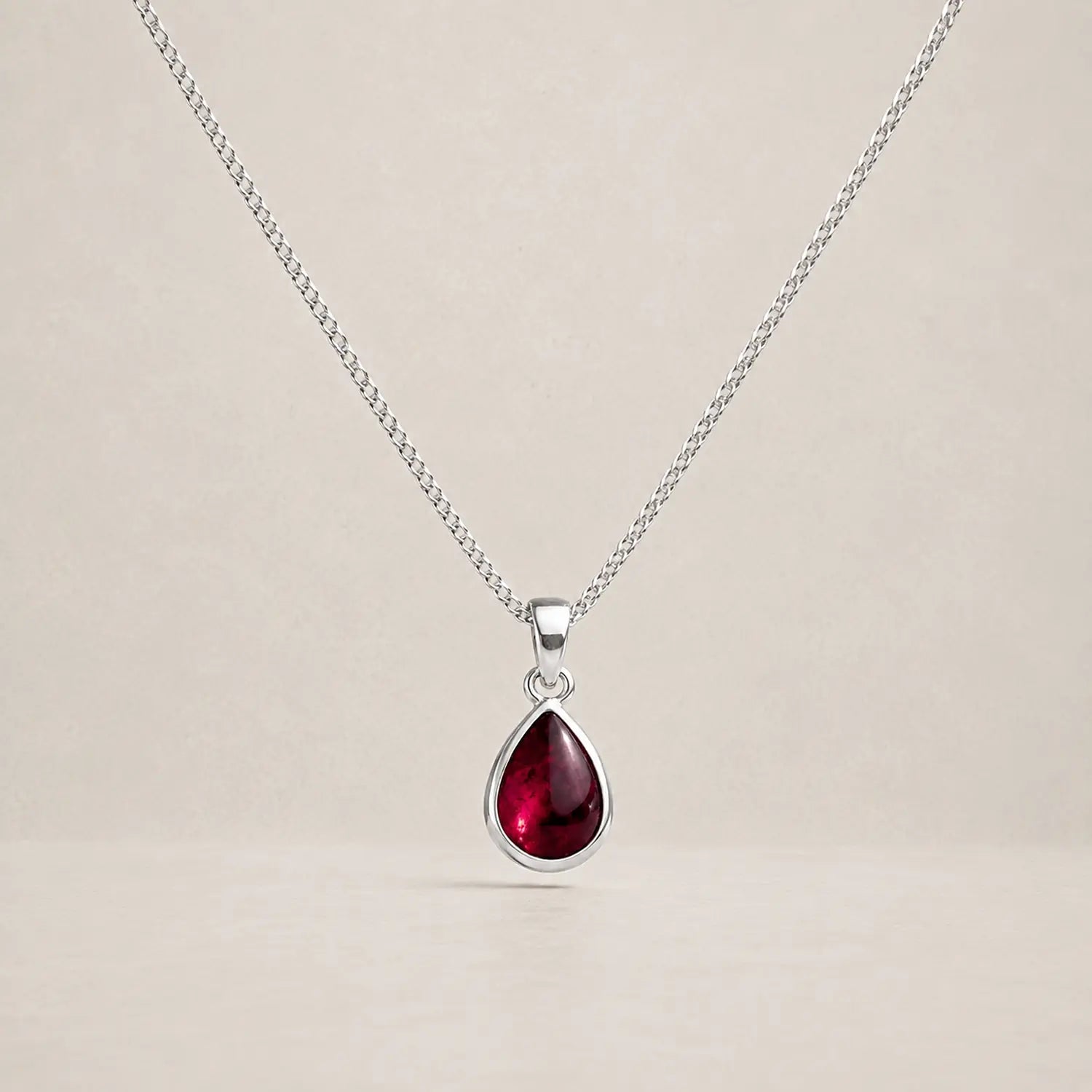 Sterling silver January birthstone necklace with a small pear-shaped garnet pendant on a pale stone background