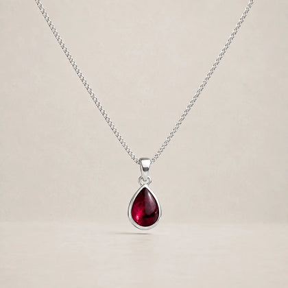 Sterling silver January birthstone necklace with a small pear-shaped garnet pendant on a pale stone background