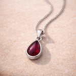 Teardrop-shaped pendant with red natural garnet gemstone on a sterling silver chain against a beige background