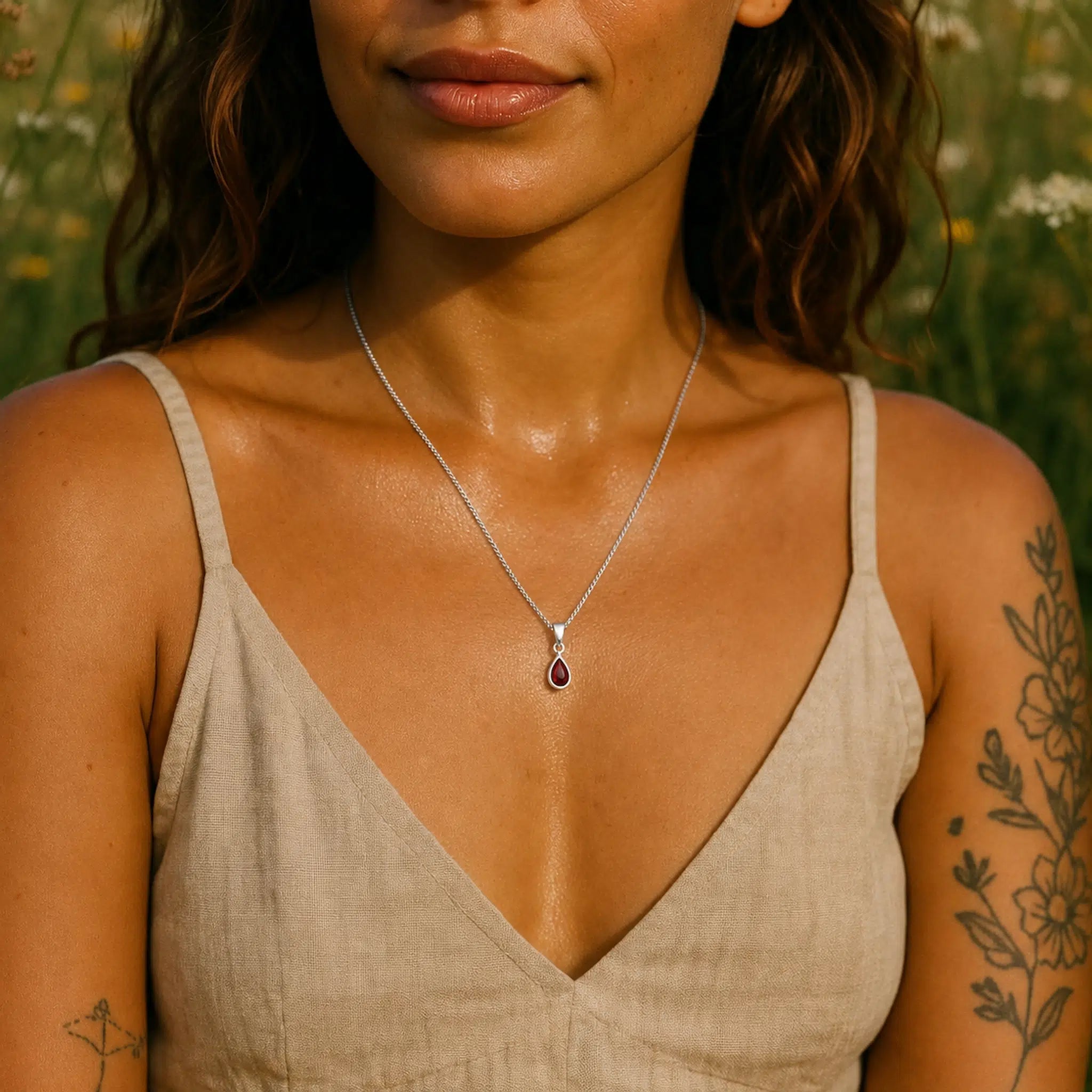 woman wearing a delicate sterling silver january birthstone necklace with a natural garnet gemstone pendant against a blurred natural background