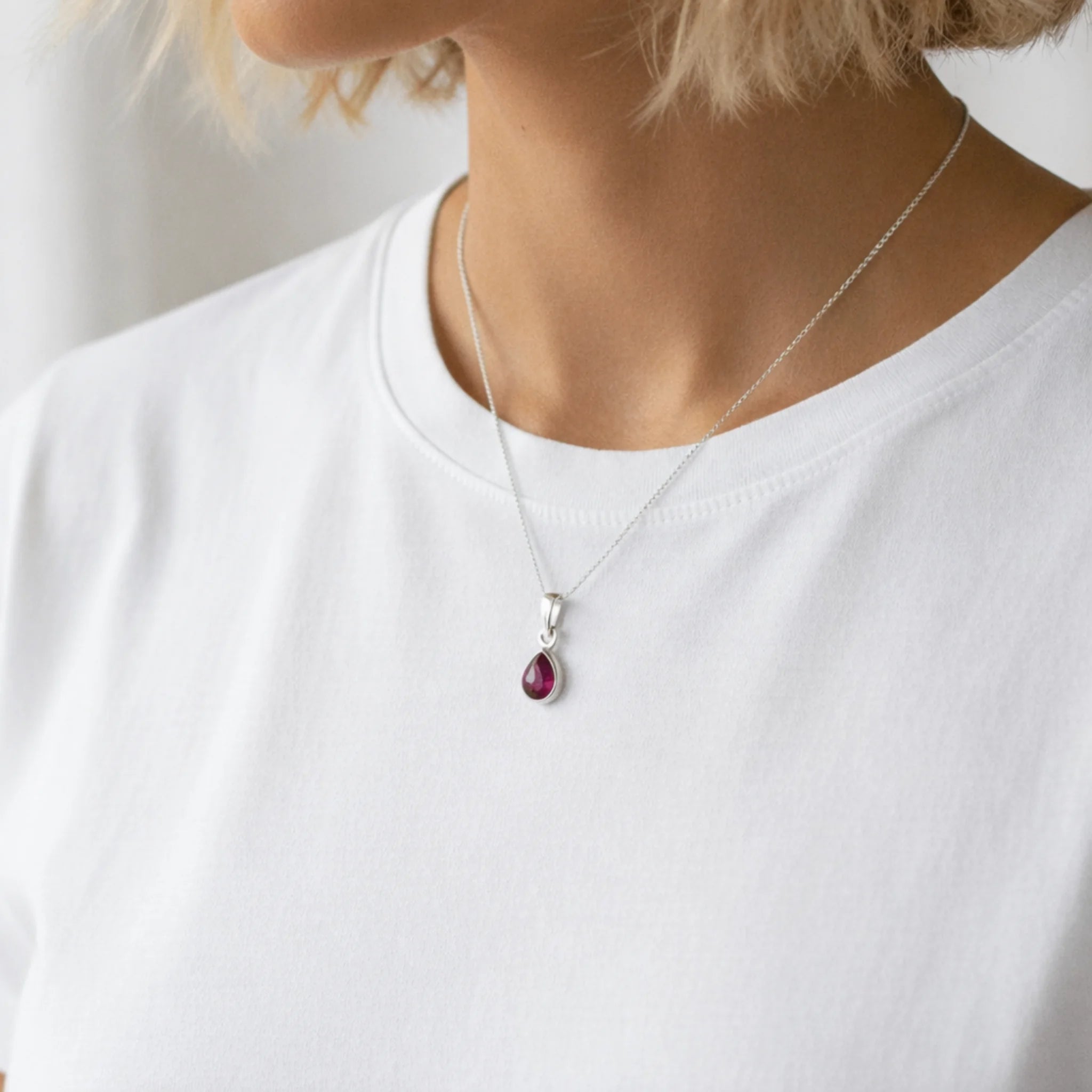 sterling silver necklace with a red teardrop natural ruby gemstone pendant worn by a person on a white background