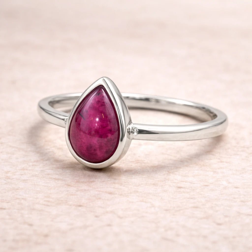 Silver ring with a natural ruby teardrop-shaped gemstone on a light pink background