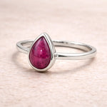 Silver ring with a natural ruby teardrop-shaped gemstone on a light pink background