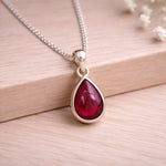 Sterling Silver necklace with a red natural ruby gemstone teardrop shaped pendant on a wooden surface