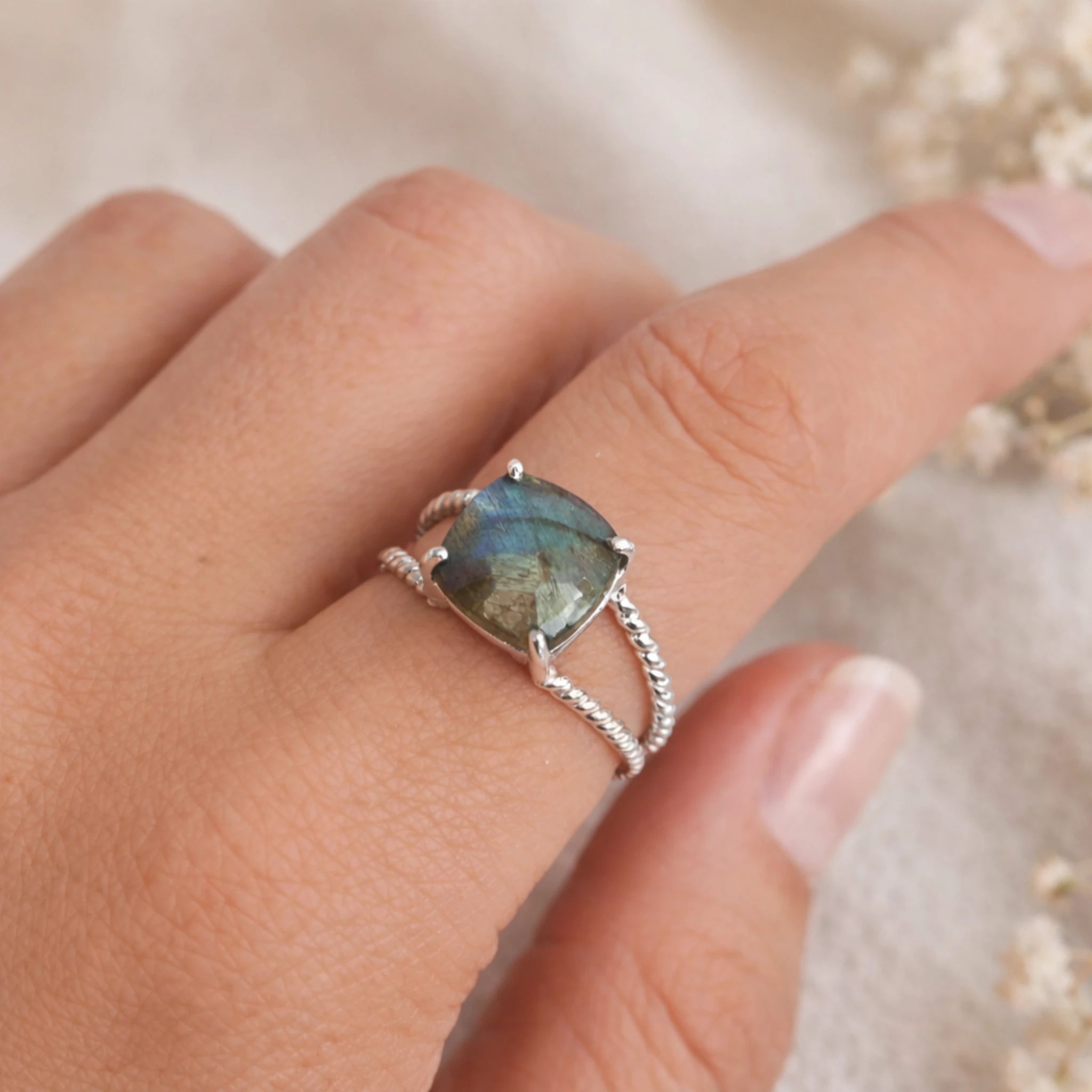 sterling Silver ring with a claw set faceted labradorite gemstone on a finger against a blurred background