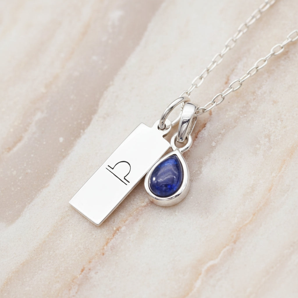 Sterling Silver necklace with a tear drop natural sapphire gemstone pendant and a libra zodiac pendant on a textured background