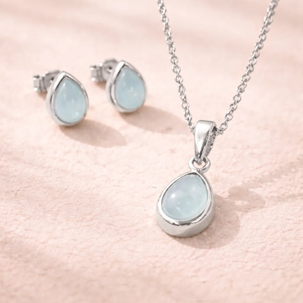 Sterling Silver Jewellery set with pear drop-shaped pendant and earrings with natural bezel set aquamarine gemstones on a soft pink background