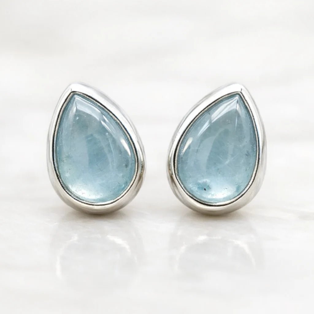 Teardrop-shaped natural aquamarine gemstone earrings with silver settings on a white background