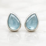 Teardrop-shaped natural aquamarine gemstone earrings with silver settings on a white background