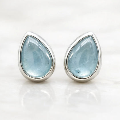 Teardrop-shaped march birthstone natural aquamarine gemstone earrings with silver settings on a white background