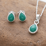 Sterling silver Jewellery set with green emerald teardrop stones on a brown stone surface