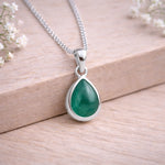 Sterling Silver necklace with a green teardrop natural emerald gemstone pendant on a wooden background