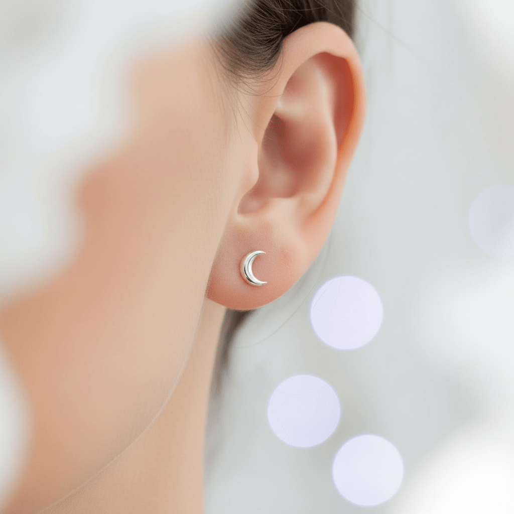 Close-up of an ear wearing a silver moon-shaped earring with a blurred background