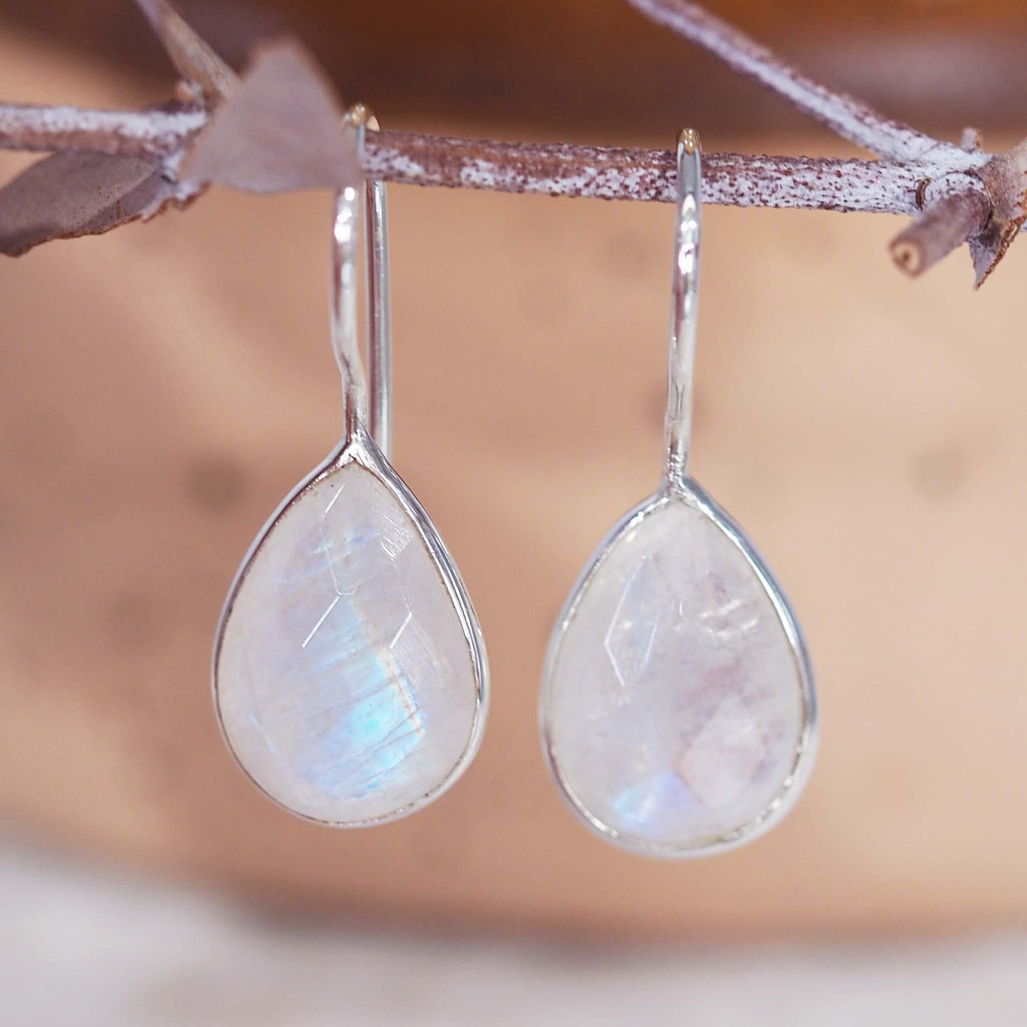 Teardrop-shaped sterling silver french hook earrings with rainbow moonstone stones on a soft background