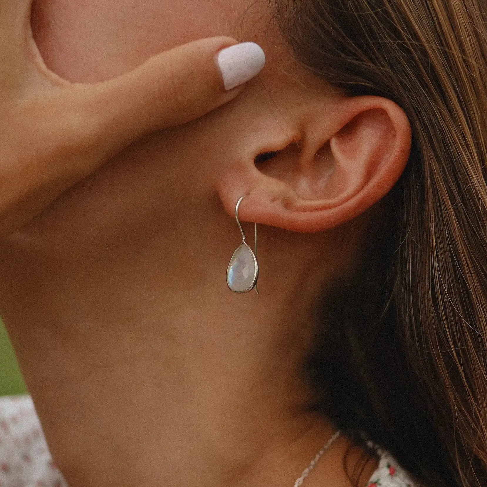 Close-up of a person wearing a sterling silver teardrop-shaped moonstone earring with a blurred background