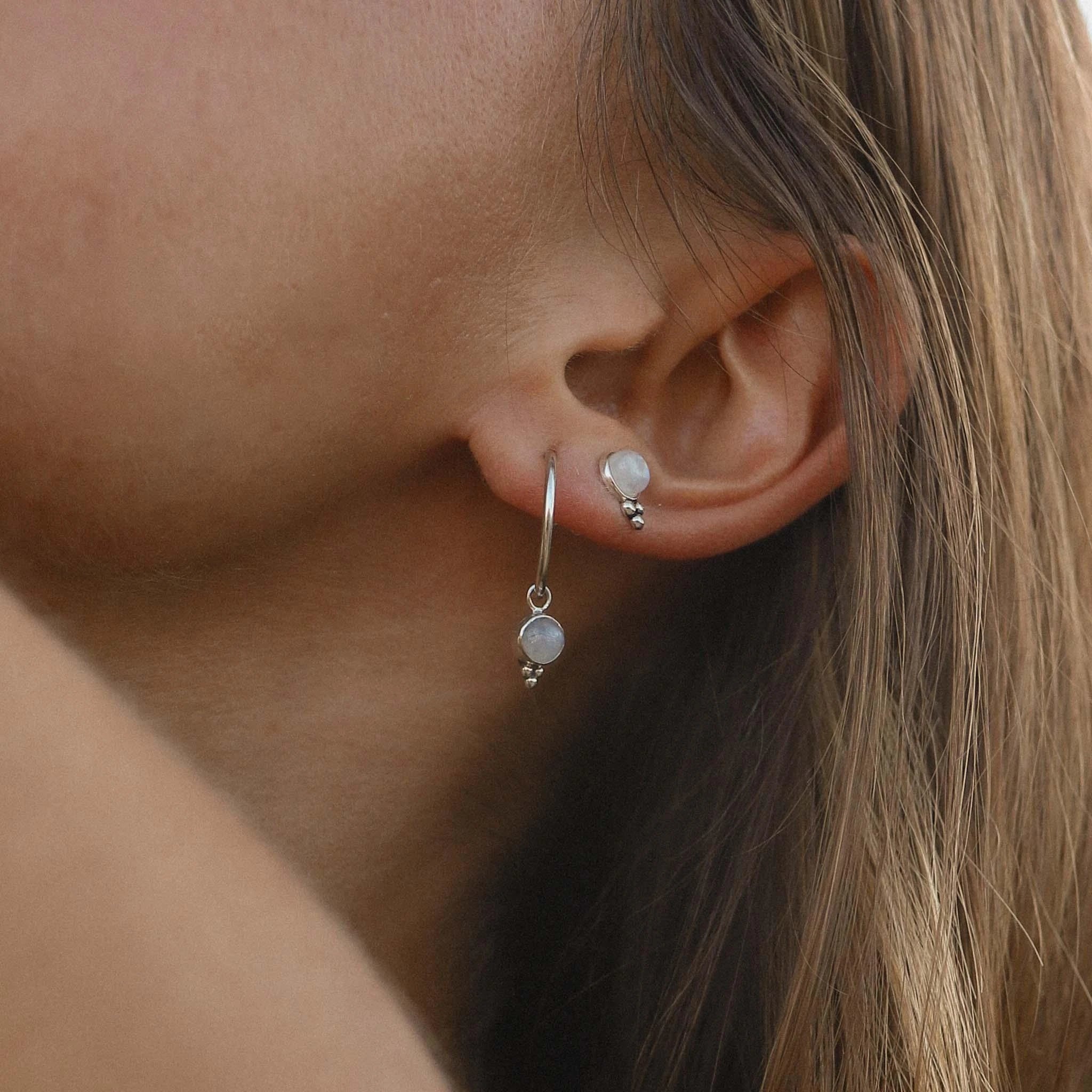 Close-up of an ear wearing sterling silver moonstone earrings with small round stones.
