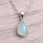 Teardrop-shaped pendant with rainbow moonstone on a silver chain against a wooden background