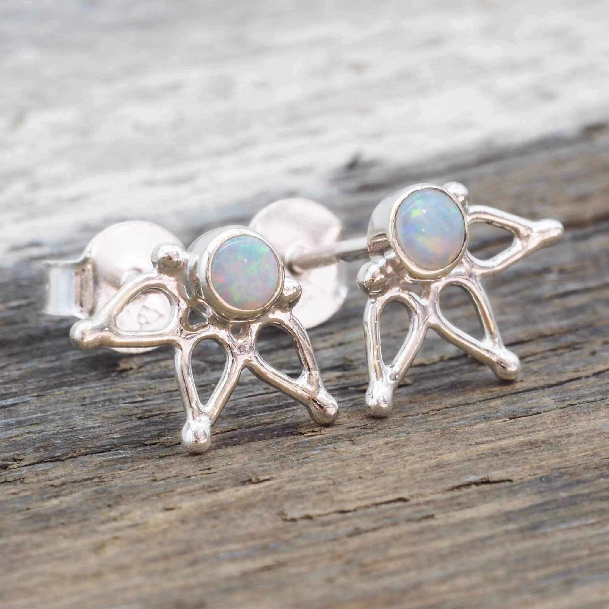 Pair of 925 sterling silver lotus stud earrings with round bezel-set natural Australian opals on a rustic wooden surface.
