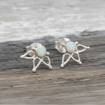 A pair of silver stud earrings with a central round white opal stone with lotus design displayed on a rustic wooden surface.