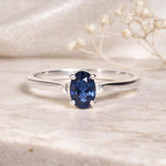 Sterling Silver Oval Claw Set faceted natural sapphire gemstone ring on a light stone surface