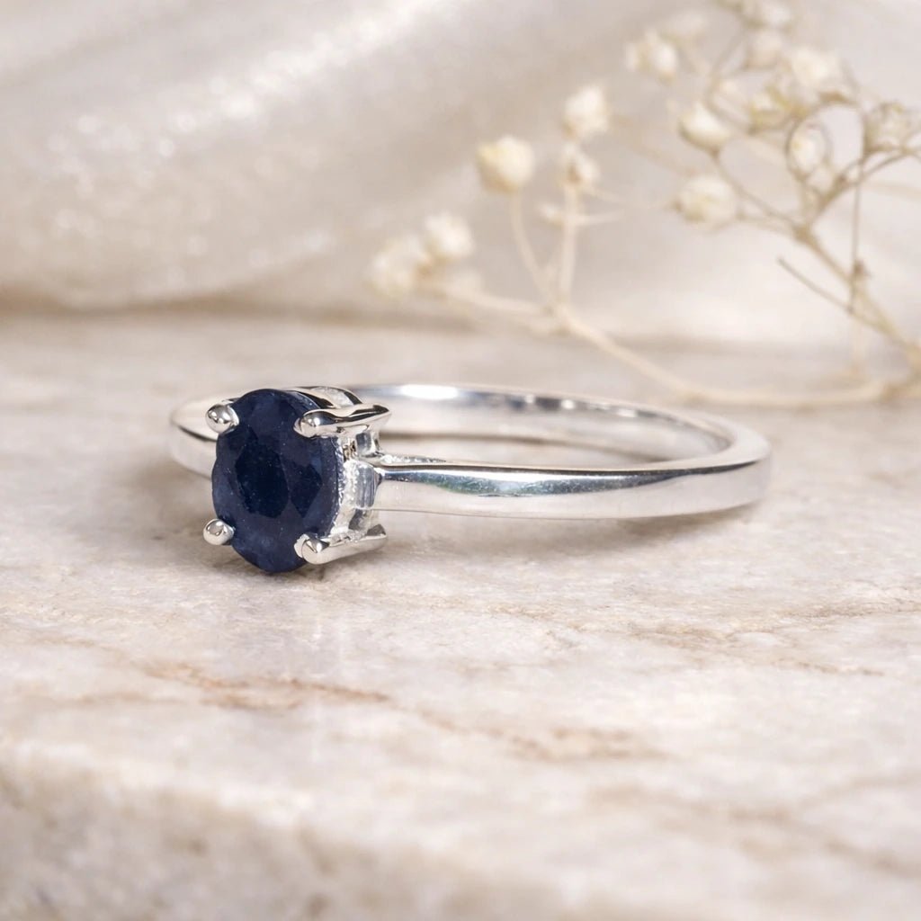 Sterling Silver Oval Claw Set faceted natural sapphire gemstone ring on a light stone surface