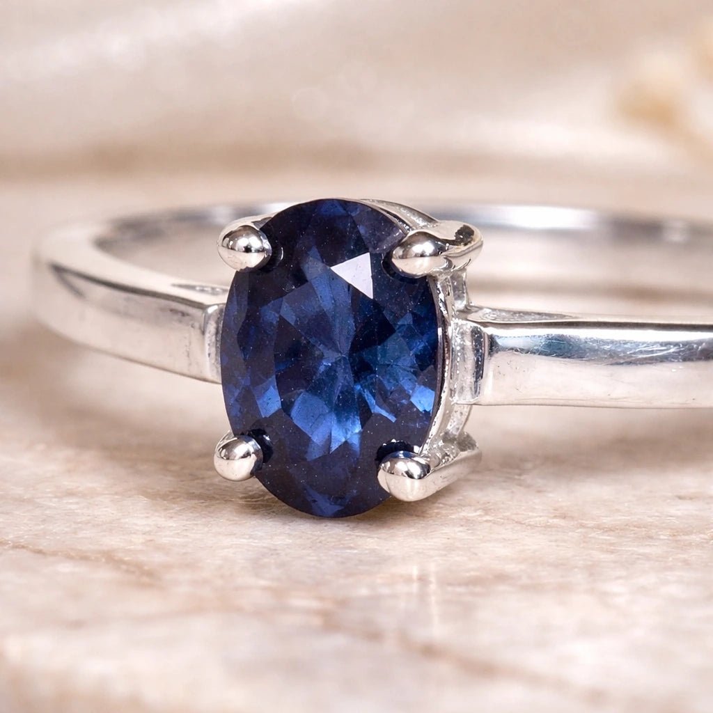 Sterling Silver Oval Claw Set faceted natural sapphire gemstone ring on a light stone surface